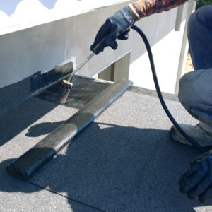 Roofer preparing part of bitumen roofing felt roll for melting by gas heater torch flame